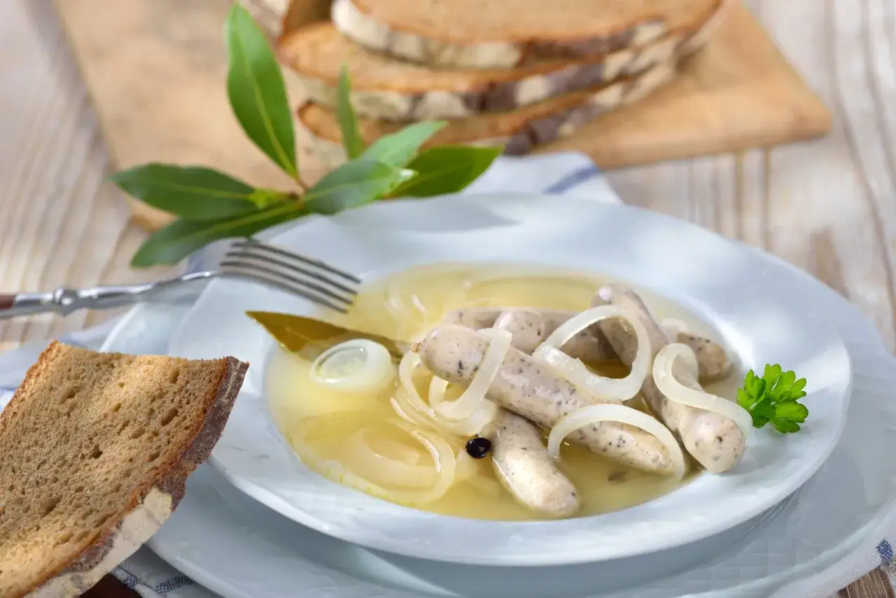 Rezept für blaue Zipfel: Würzige Bratwürste in einer Brühe mit Zwiebeln, Lorbeer und Pfeffer, serviert mit Brot.
