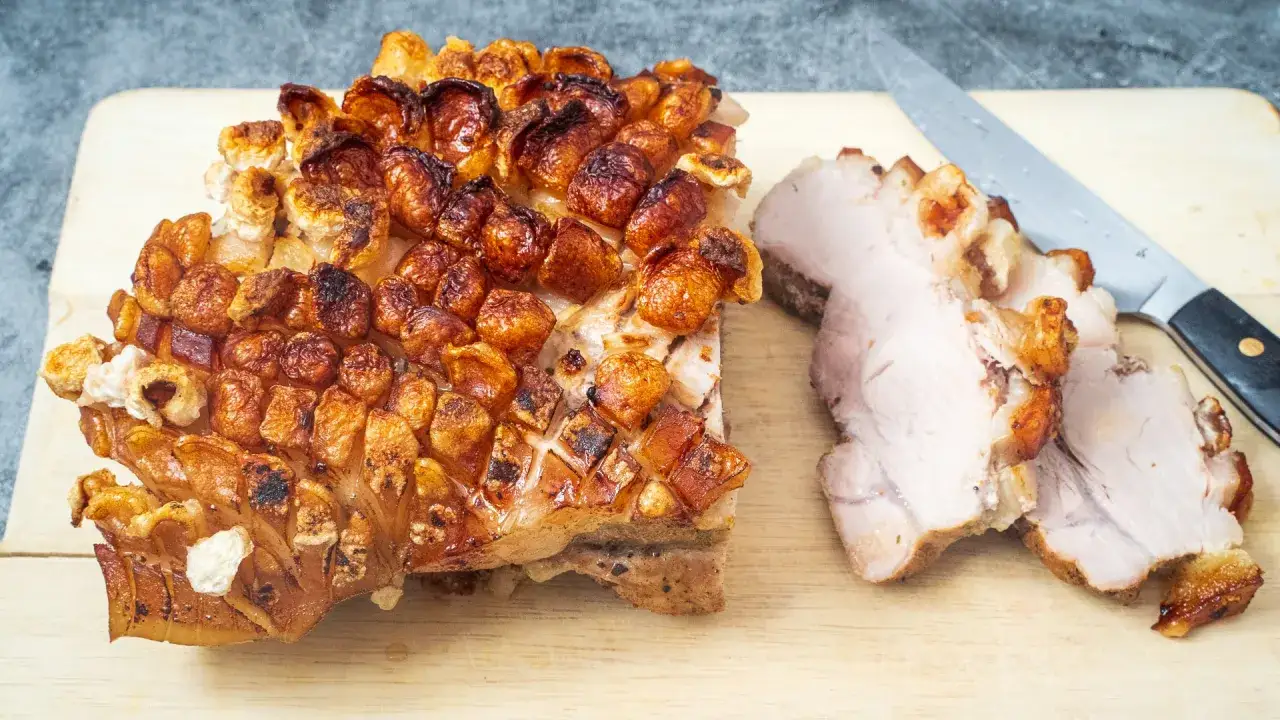 Ein knuspriger Schweinebraten mit Kruste, daneben aufgeschnittenes Fleisch und ein Messer.