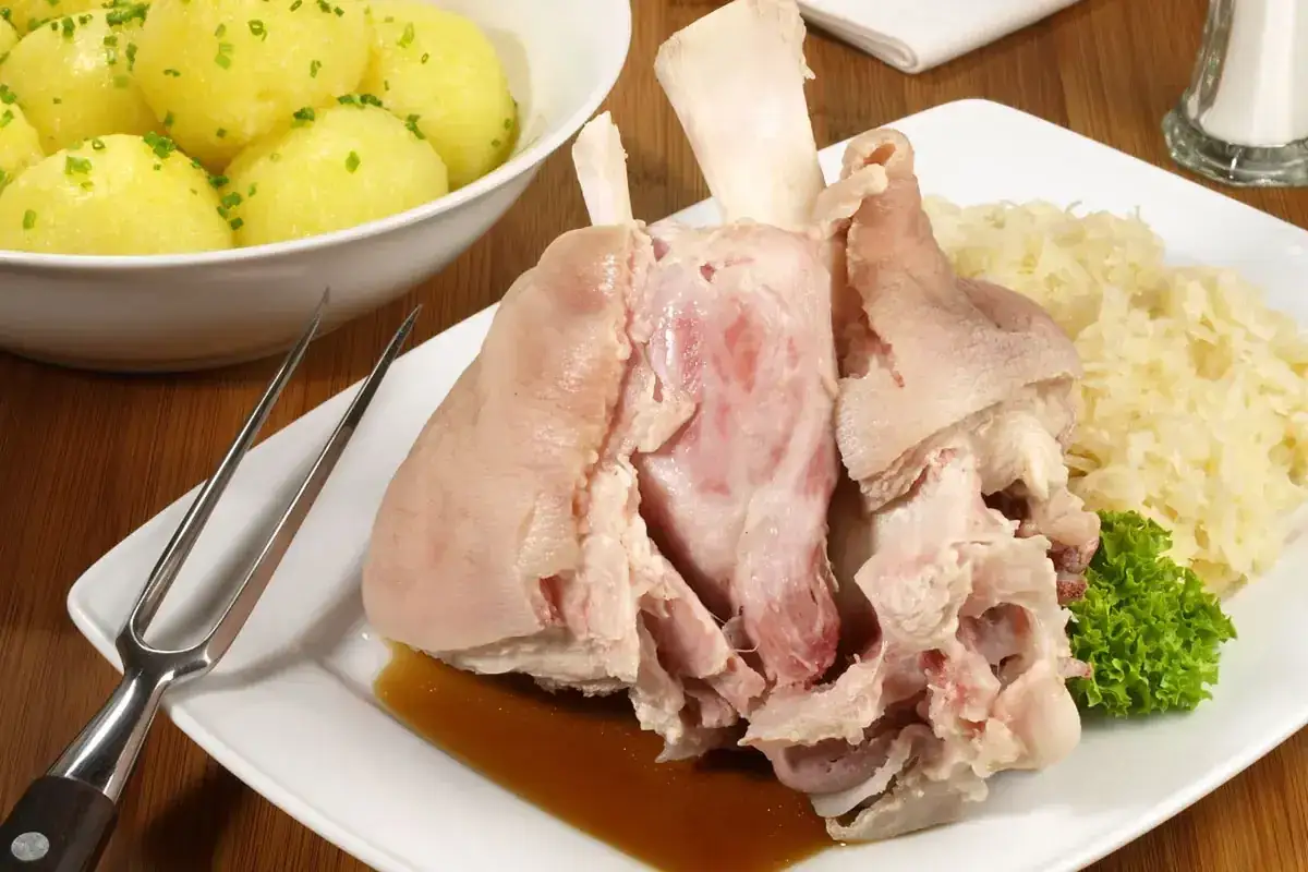 Ein deftiges Eisbein in Sauerkraut kochen, serviert mit Salzkartoffeln und einer Gabel.