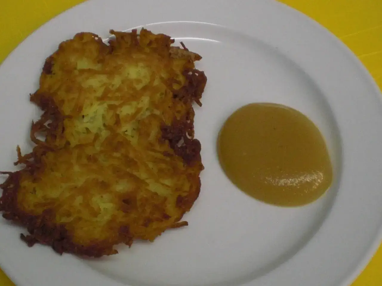 Zwei knusprige Kartoffelpuffer liegen auf einem Teller neben einem Klecks Apfelmus.