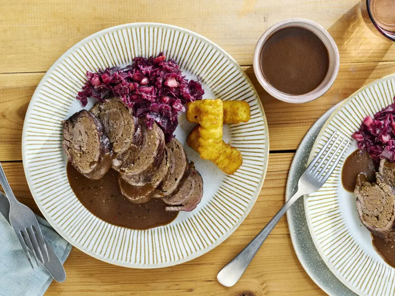 Zwei Teller mit deftigen deutschen Gerichten: Rouladen in dunkler Sauce, Rotkohl und Kroketten.