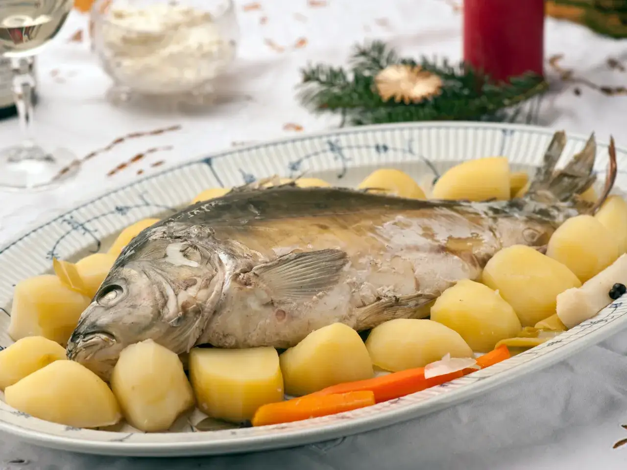 Ganzes Karpfengericht mit Salzkartoffeln und Karotten auf einem ovalen Teller, festlich dekoriert.
