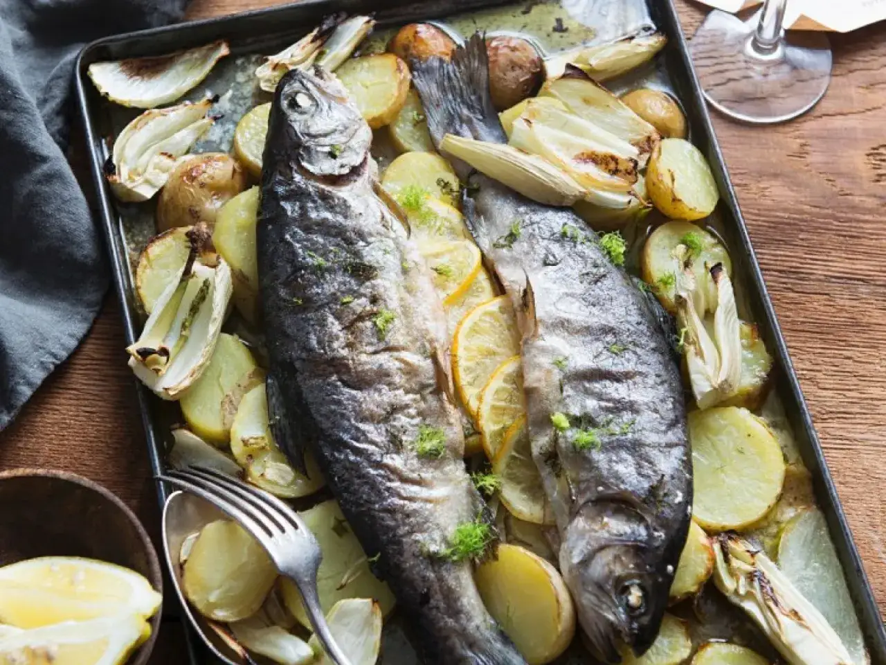 Zwei ganze Forellen im Backofen mit Kartoffeln, Fenchel und Zitronenscheiben auf einem Blech.