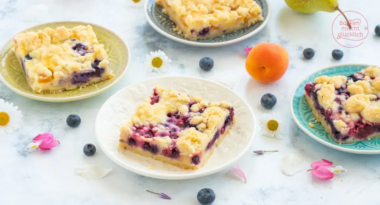 Saftiger versunkener Streuselkuchen mit Blaubeeren und Aprikosen auf Tellern, dekoriert mit frischen Beeren und Blüten.