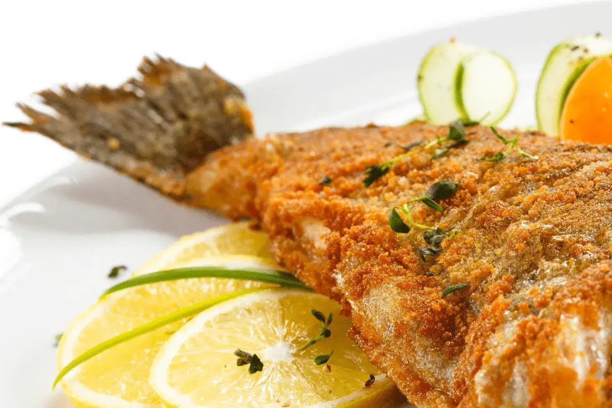 Knusprig gebratener Fisch, ein Klassiker der Karpfen Gerichte, serviert mit Zitronenscheiben und Kräutern.