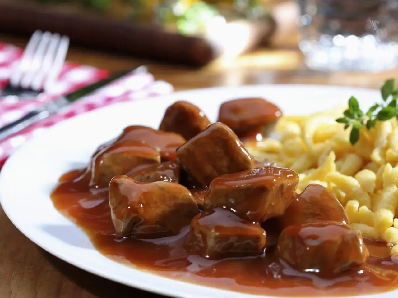 Ein Teller mit saftigem Kalbsgulasch in dunkler Sauce, serviert mit Spätzle. Ein köstliches Kalbsgulasch Rezept zum Nachkochen.