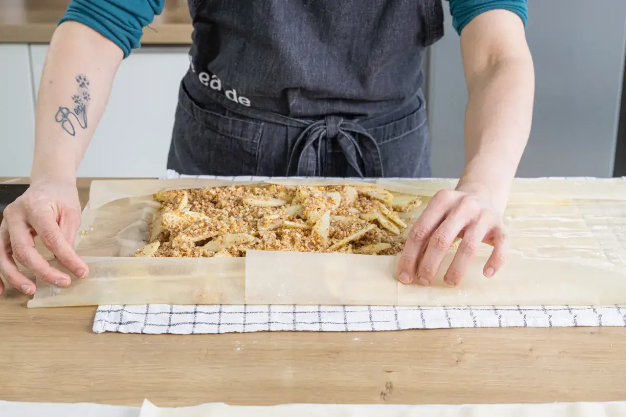 Hände formen einen Apfelstrudel mit fertigem Strudelteig, gefüllt mit Äpfeln und Nüssen.