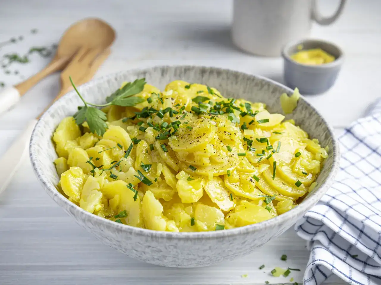 Schüssel mit cremigem Kartoffelsalat, garniert mit Schnittlauch und Petersilie. Ein klassisches rezept kartoffelsalat, bereit zum Servieren.