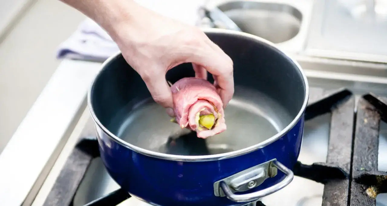 Hand legt Rinderroulade in blauen Topf. Man muss Rinderrouladen nicht waschen, sie werden direkt zubereitet.