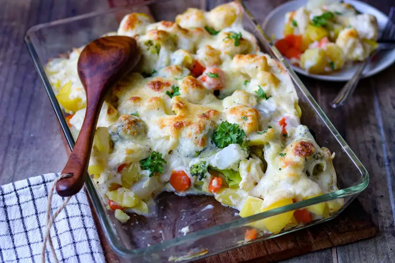 Ein köstlicher vegetarischer Auflauf mit Kartoffeln, Brokkoli, Blumenkohl und Karotten, überbacken mit geschmolzenem Käse und garniert mit Petersilie.
