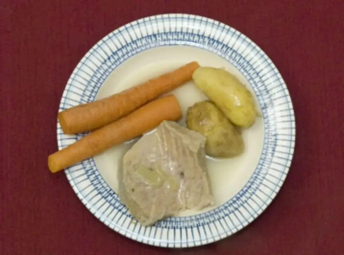 Ein Teller mit gekochtem Rindfleisch, Karotten und Kartoffeln. Ein herzhaftes Gericht, das an Omas Küche erinnert.