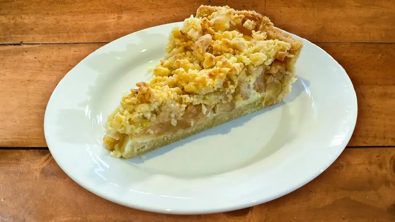 Ein Stück Florentiner Apfelkuchen mit knuspriger Streuseldecke auf einem weißen Teller.