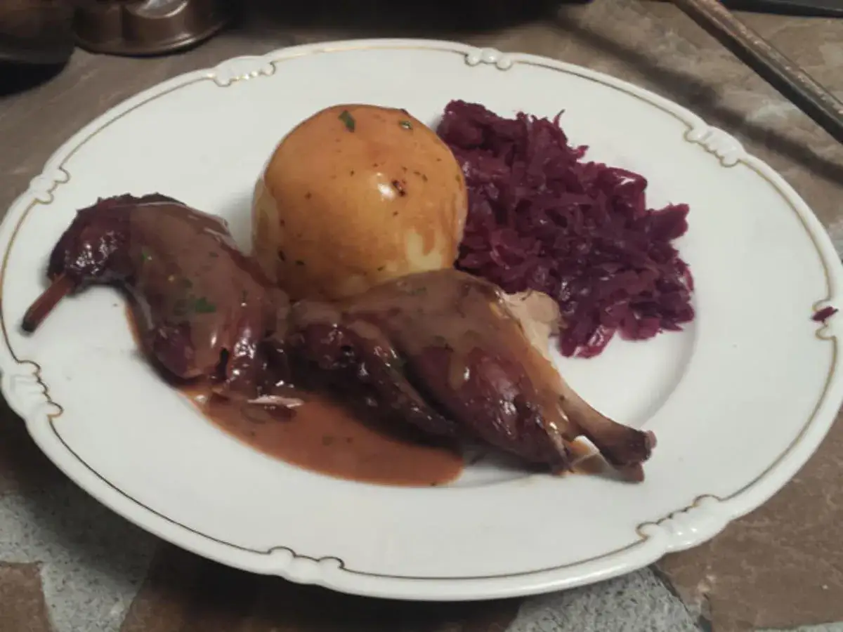 Ein festliches Karnickel-Rezept: Zwei gebratene Karnickel mit Sauce, dazu ein Kartoffelklops und Rotkohl auf einem Teller mit Goldrand.