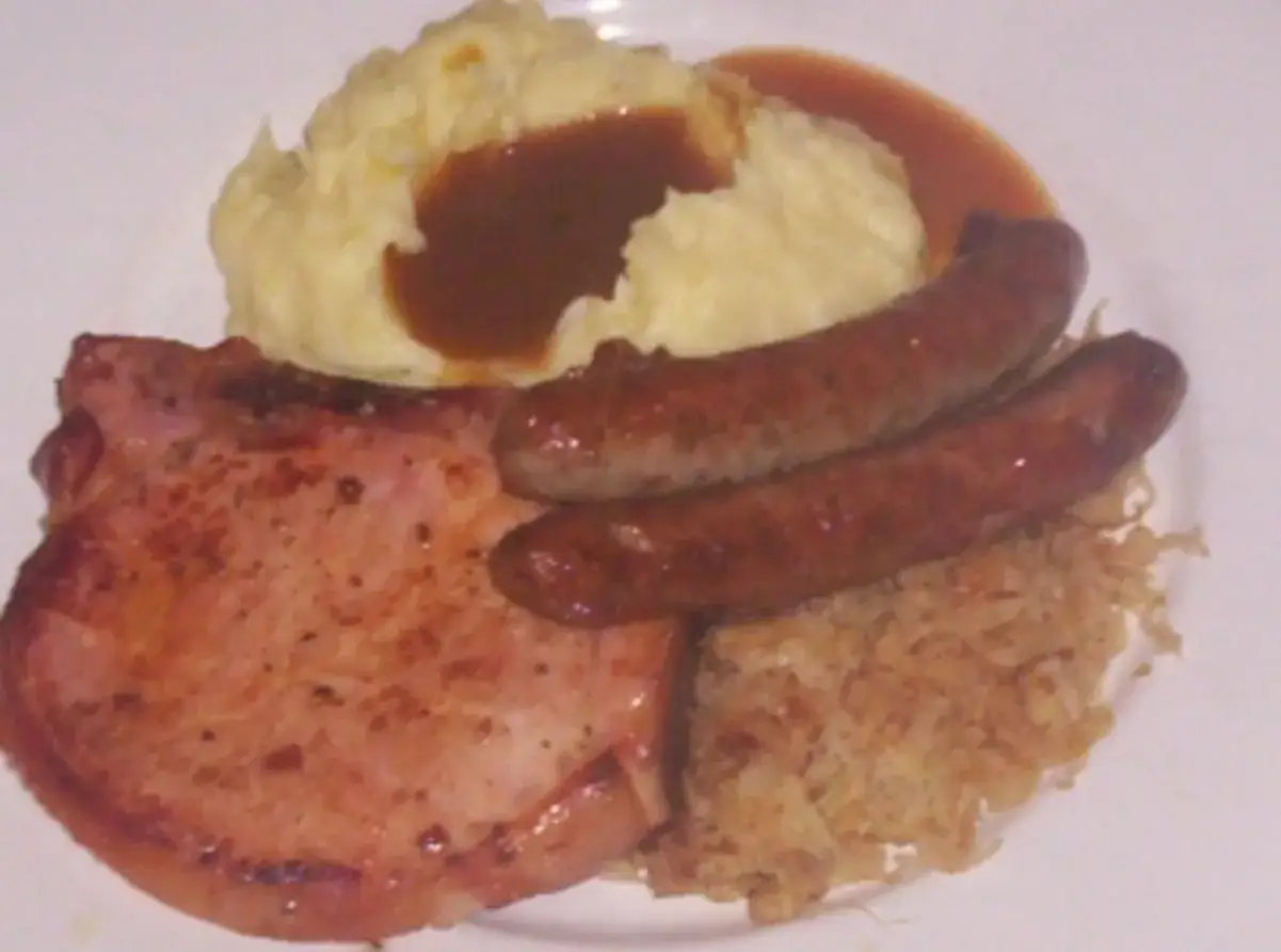 Herzhaftes Gericht mit Schweinekotelett, zwei Würstchen, Kartoffelpüree mit Soße und gebratenem Sauerkraut.