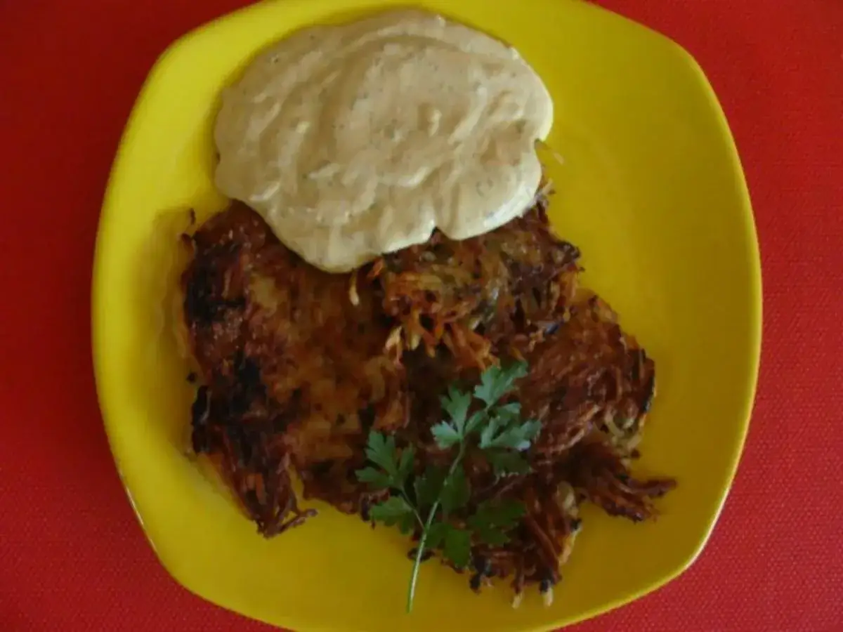 Knusprige Kartoffelpuffer mit einer cremigen Sauce und einem Hauch von Fleisch, garniert mit Petersilie auf einem gelben Teller.