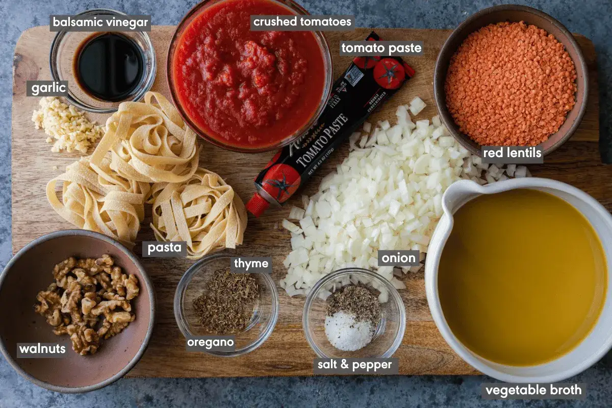 Zutaten für eine herzhafte Linsen Bolognese: rote Linsen, Pasta, Tomaten, Zwiebeln, Knoblauch, Walnüsse, Gewürze und Brühe.