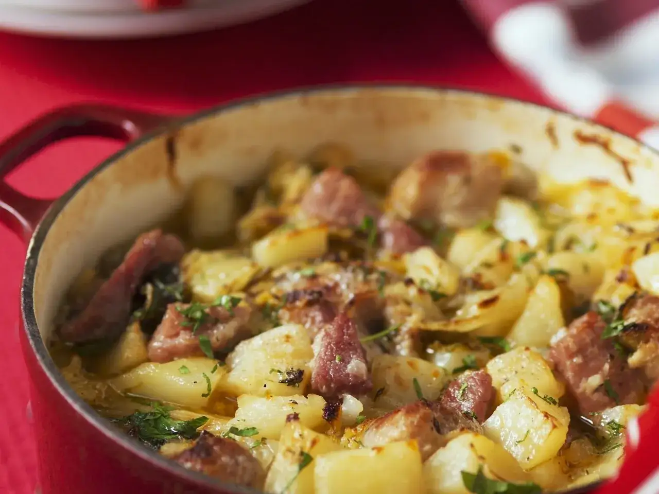 Herzhaftes Bamberger Wirsing Rezept mit Kartoffeln und Wurststücken, frisch aus dem roten Bräter, garniert mit Petersilie.