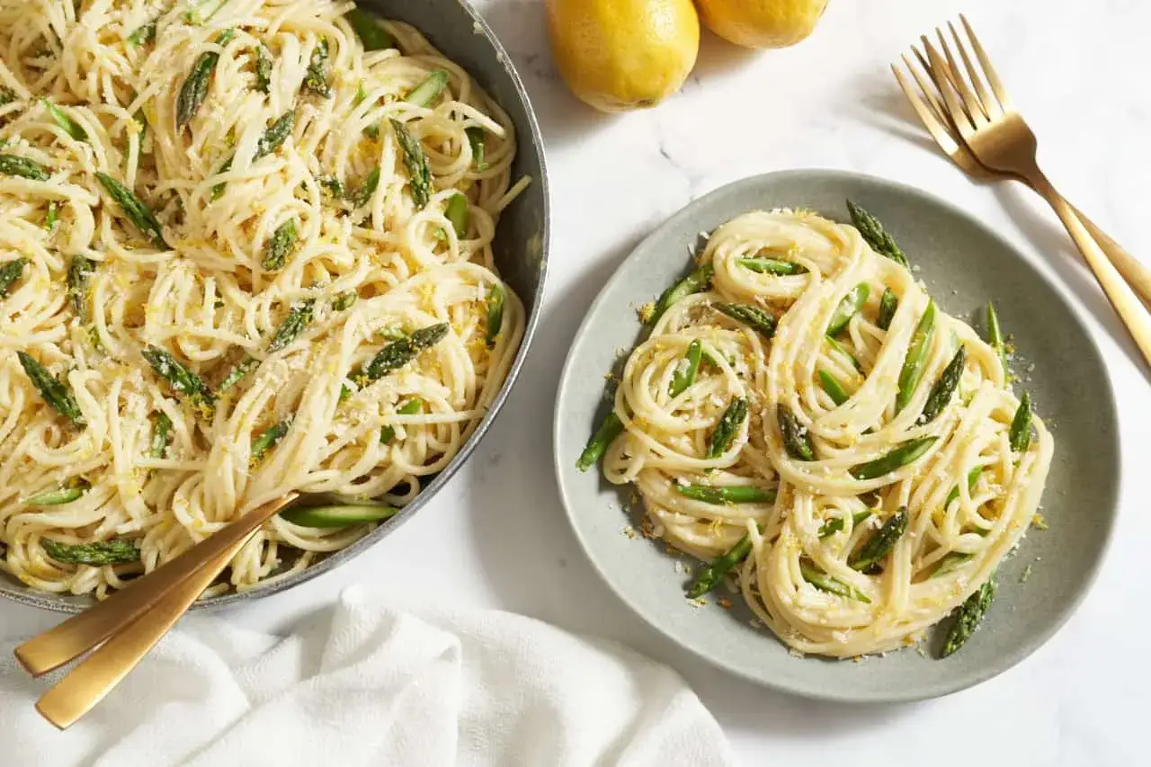 Spargel Pasta mit Zitrone und Parmesan. Ein Teller voller cremiger Spaghetti mit frischem Spargel, garniert mit Zitronenschale und Käse.