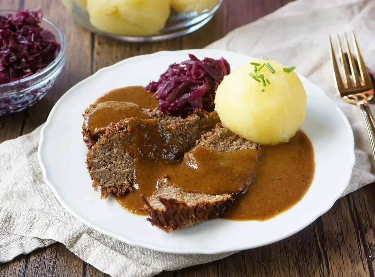 Original Sauerbraten: zartes Rindfleisch in dunkler Sauce, serviert mit Rotkohl und Klößen.