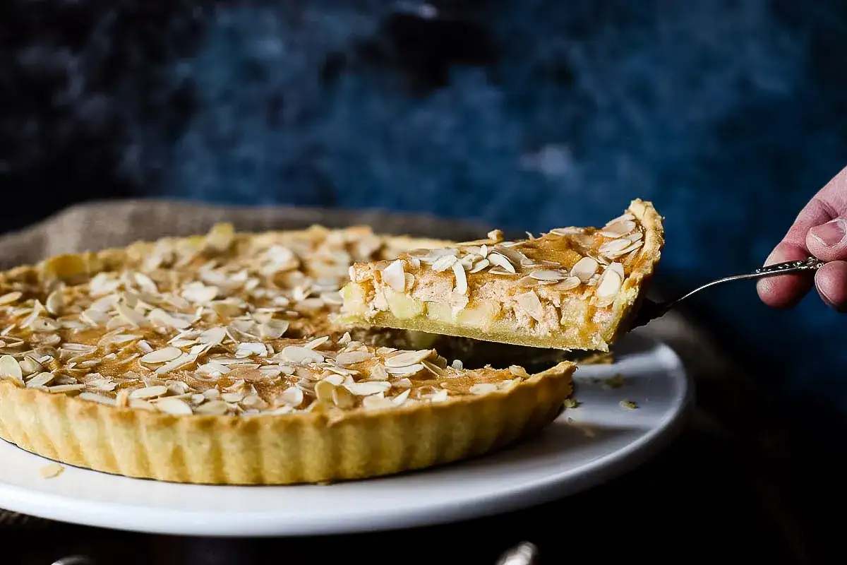Ein Stück einer sensationellen Apfeltarte mit Mandelblättchen wird herausgehoben.