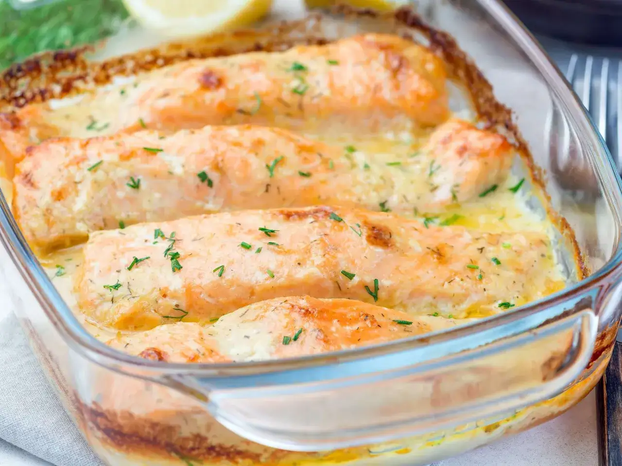 Vier saftige Lachsfilets in cremiger Sahnesauce, überbacken und mit frischen Kräutern bestreut. Ein köstliches Lachs Sahne Gratin, bereit zum Genießen.