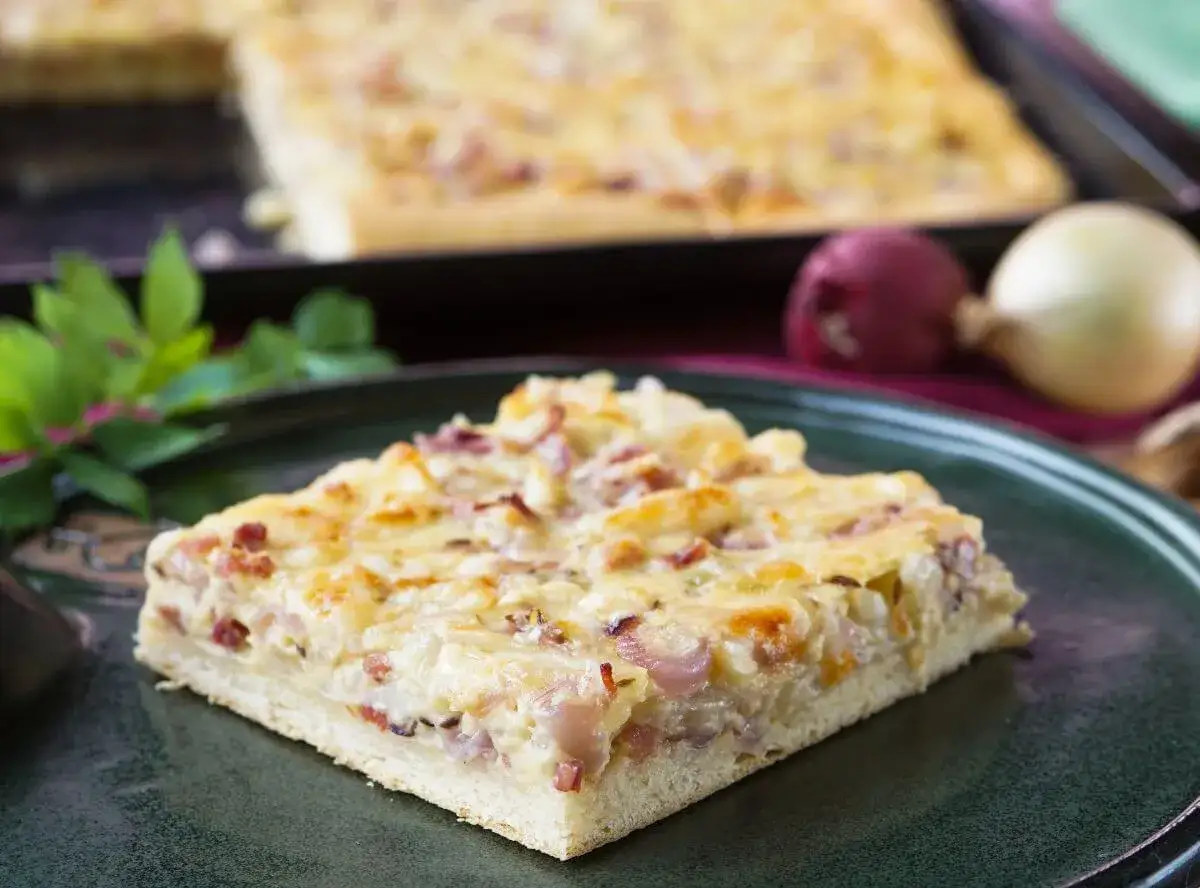 Ein Stück herzhafter Zwiebelkuchen mit Speck und Käse auf einem Teller. Das Rezept für diesen Klassiker ist einfach und gelingt immer.