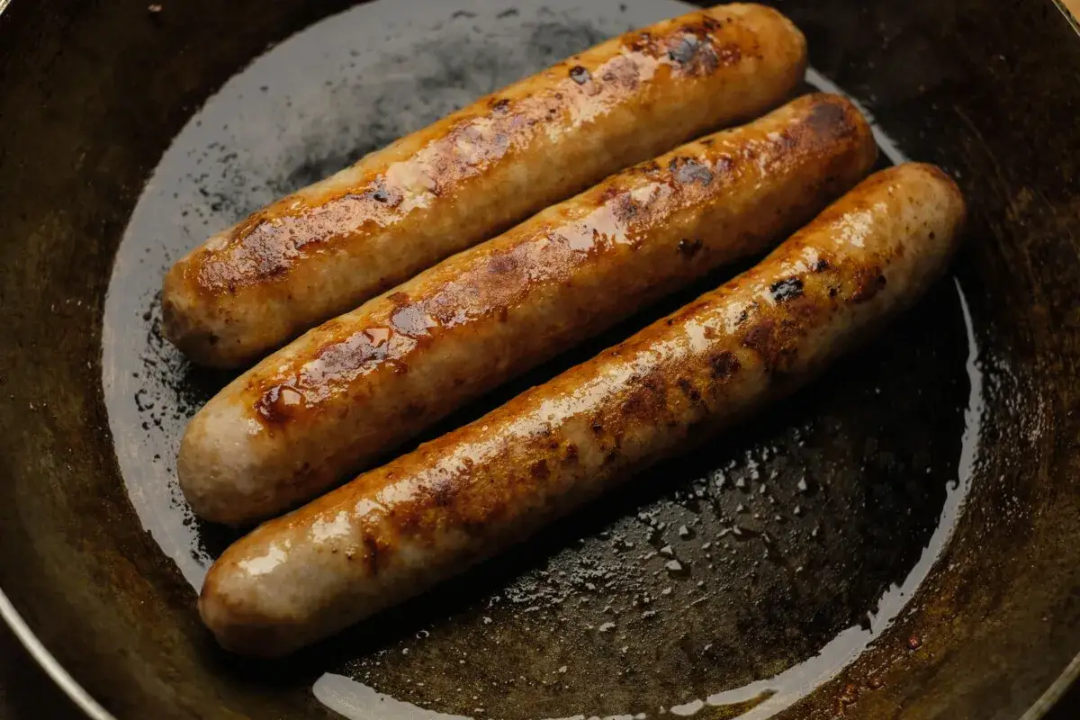 Drei rohe Bratwürste braten in einer Pfanne, goldbraun und saftig.